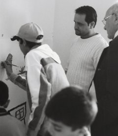 <p>Iraqi artist Amer
watches as boy works on mural, and unidentified man in
suit watches, Webdah School, May 2007</p>